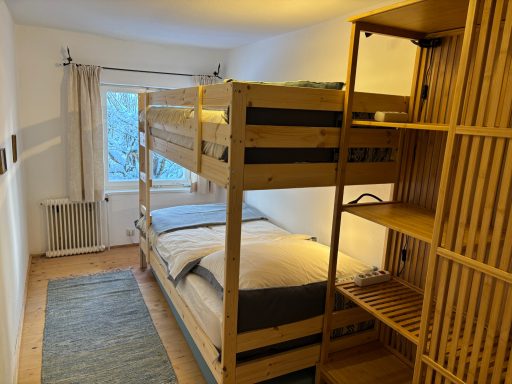 Helles Zimmer mit Etagenbett, zwei Betten und Holzregal.