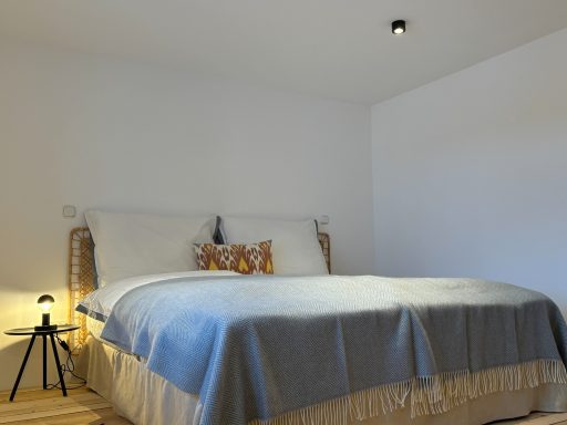 Helles Schlafzimmer mit einem großen Bett, kuscheliger Decke und minimalistischer Dekoration.