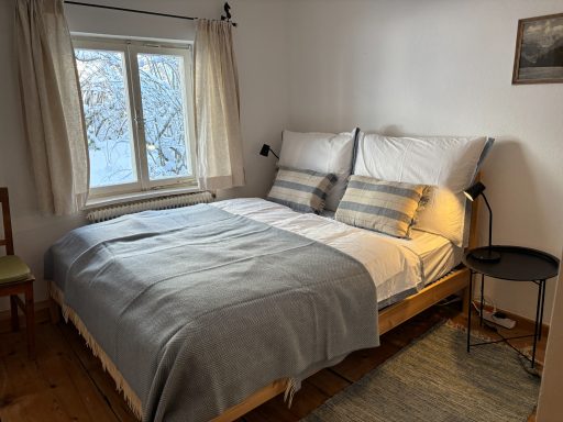Gemütliches Schlafzimmer mit einem Doppelbett, Fenster und Holzstuhl.