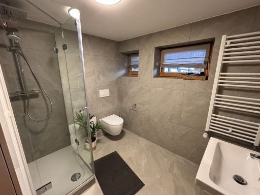 Modernes Badezimmer mit Dusche, Toilette, Waschbecken und Fenster.
